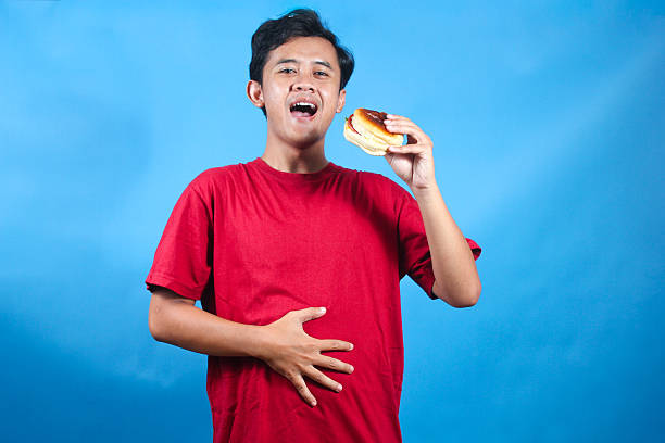 Asian man holding hamburger while rubbing his stomach