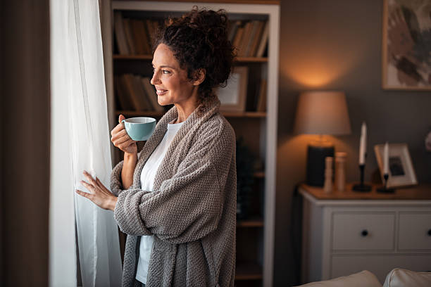 istock Cozy Morning Moment: Woman In Robe Sips Cup By Window At Home, Smiling 2252452005