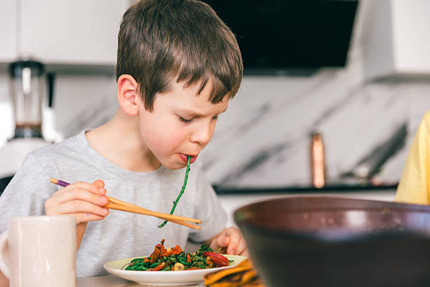 istock Little boy eating green noodles with chopsticks at home kitchen table 2252470118