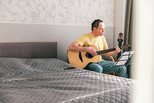 istock Man practicing acoustic guitar at home with sheet music stand 2252471500