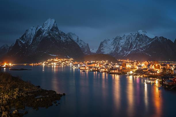 istock Night Lakeside with Houses, Reflections, and Snow-Capped Mountains 2252475444