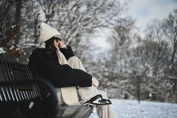 istock Young woman enjoying cold winter day while sitting on park bench 2252478619