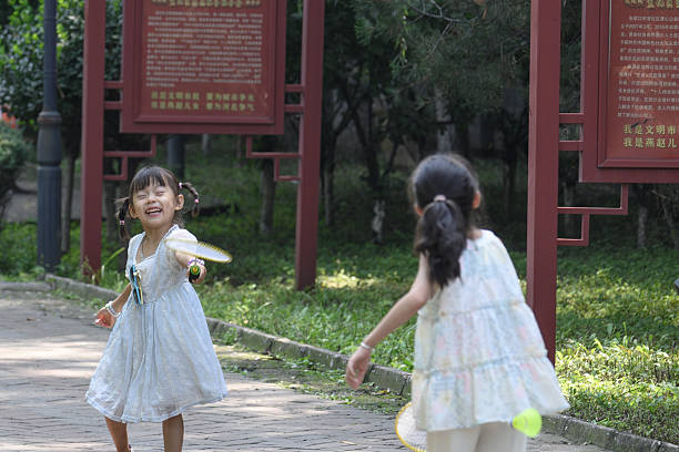 Three elementary children, African-American girl and two Asian kids playing together in a grass field surrounded by trees and bubbles, outdoors playing, laughing and enjoying a carefree day in nature