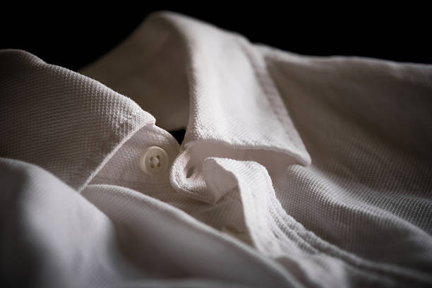 Soft, moody close-up of white shirt, highlighting its smooth fabric, subtle folds and button near collar. Gentle lighting emphasizes the texture and elegance of the material