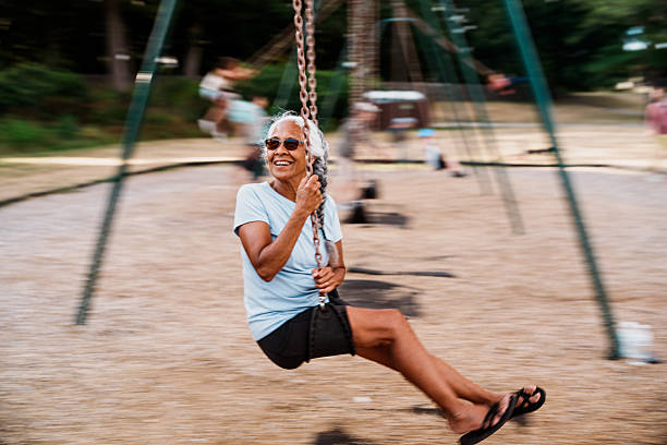 An active senior woman of Hawaiian and Chinese descent joyfully swings at a playground during an outing with her multi-generation family.