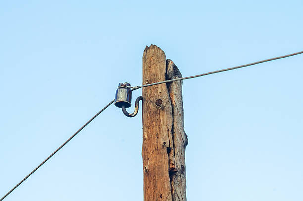 istock Weathered wooden utility pole with ceramic insulator and overhead wire against a clear blue sky 2252493675