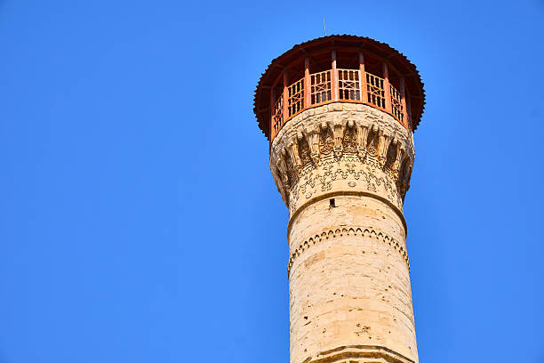 Low-angle view of ornate historic minaret rising against clear blue sky. Traditional Islamic architecture, detailed stonework, cultural heritage, religion, architectural history. Gaziantep, Turkey