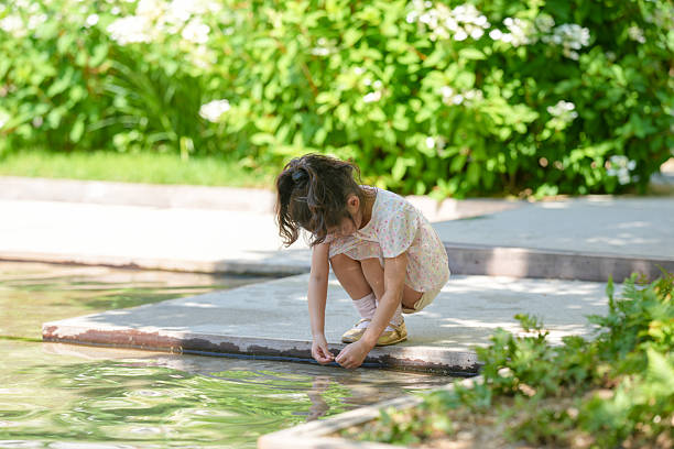A young girl is playing in a pool. She is wearing a white dress and is looking at the water