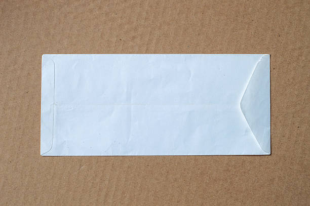 Back side behind rear of clean white colored textured long paper blank empty envelope with placed over brown corrugated cardboard background.