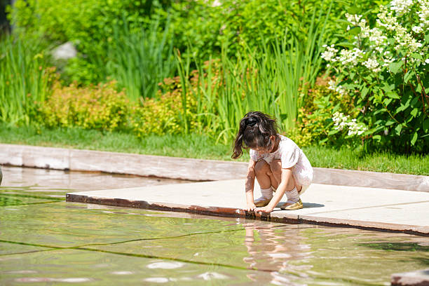 A little girl is playing in a pool. She is wearing a white dress and is kneeling in the water