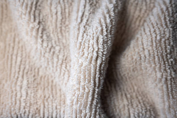 Macro close-up of a soft, beige terry cloth towel. The plush, looped texture is shown in selective focus, creating a cozy and warm abstract background for wellness or home concepts.