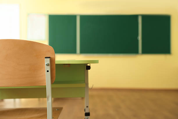 Desk with chair and green chalkboard in classroom, selective focus