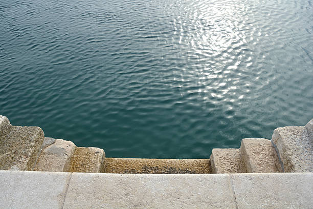 Stone steps descend into the clear blue Adriatic sea with the sun reflecting on the rippling water surface during a bright day