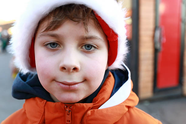 Boy in a red and white winter hat with ear flaps smiling at the camera outdoors. Portrait of young child for seasonal and holiday content.
