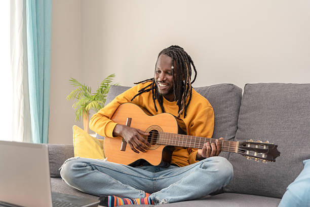 istock Smiling African american man with dreadlocks practicing guitar using an online lesson on a laptop 2252518637