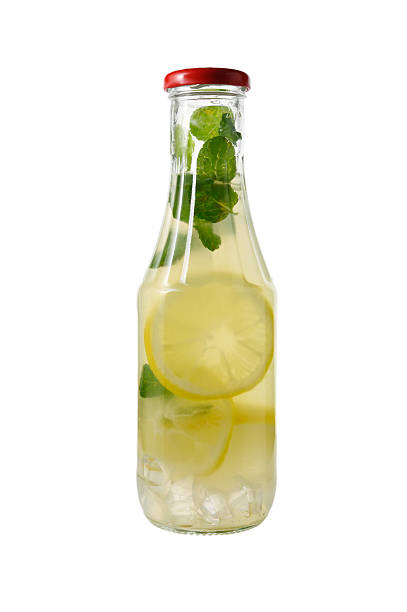 Elegant glass bottle with cork stopper containing fresh lemonade with lemon slices, mint leaves and ice, isolated on pure white background. Artisanal beverage photography.