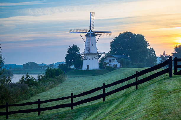 Traditional Dutch windmill De Vlinder stands silhouetted against a colorful sunrise sky in the Netherlands, capturing the calm beauty of a quiet morning in the countryside.