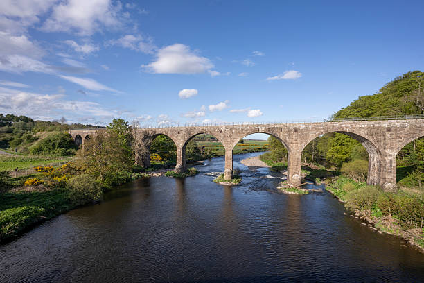 istock Historic Stone Arch Bridge Over a Quiet River in Lush Countryside Under Blue Sky 2252526671