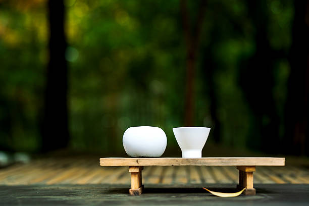 Two white ceramic tea cups on a small wooden stand against a lush, blurred green forest background.