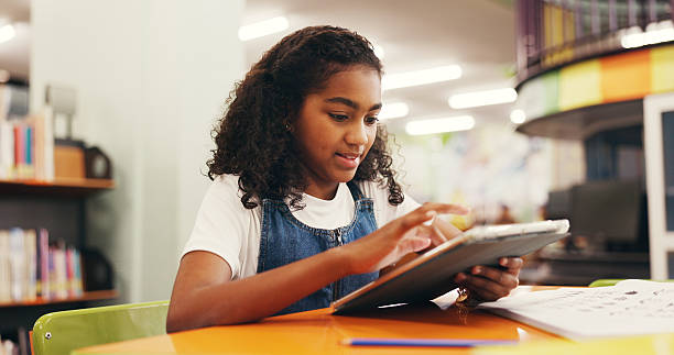 istock Tablet, education and child in library for research online with studying for test, assignment or exam. Digital technology, learning and girl kid student reading information on app for knowledge. 2252537892