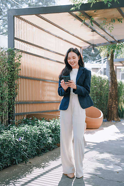 Asian businesswoman walking outdoors using smartphone and smiling