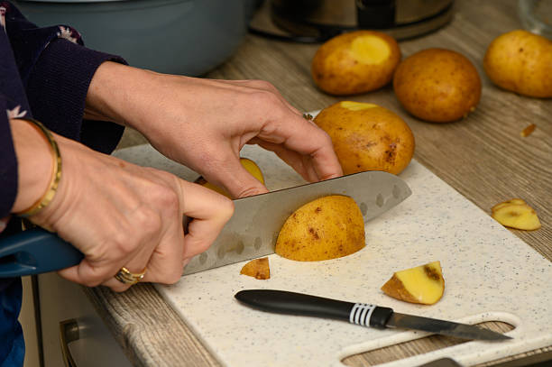 istock Close-Up of Hands Slicing Potatoes with Blue Handle Knife 2252541623