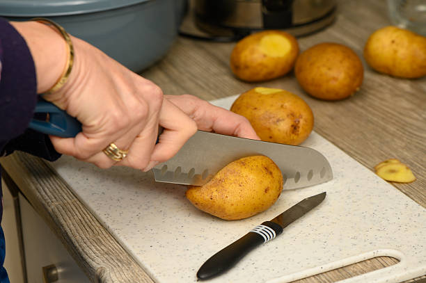 istock Woman Cutting Potatoes with Blue-Handled Knife on Board 2252544278