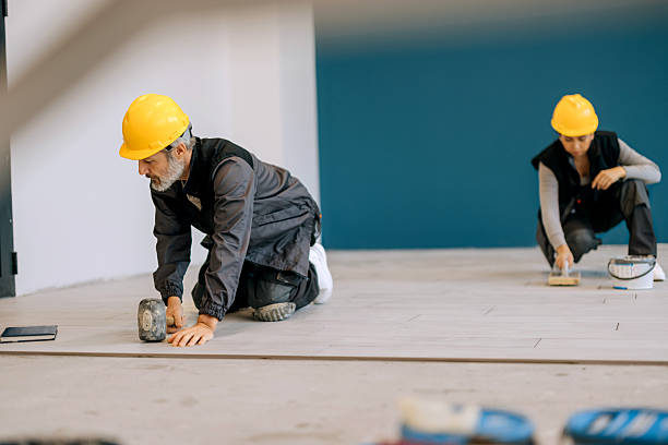 istock Floor tile worker using wooden hammer with coworker behind 2252548147