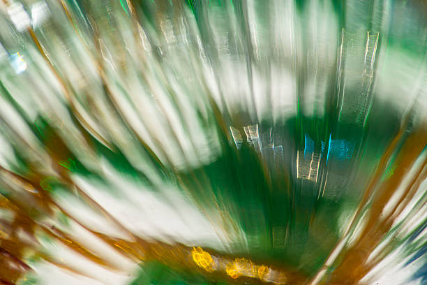 Radiating streaks of refracted glass blend white light with deep green and amber tones, forming vertical motion, soft blur, and glowing highlights in an abstract composition across the frame