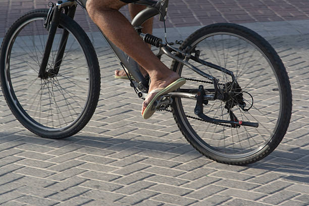 Salvador, Bahia, Brazil - December 12, 2025: Detail of the legs and wheels of a person riding a bicycle on a stone boardwalk on the Barra beach in Salvador, Bahia.
