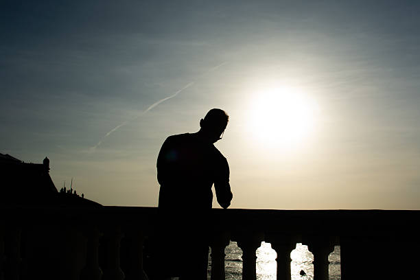 Salvador, Bahia, Brazil - December 12, 2025: A man, in silhouette, is seen walking along the shore of the Barra Lighthouse during sunset. Salvador, Bahia.