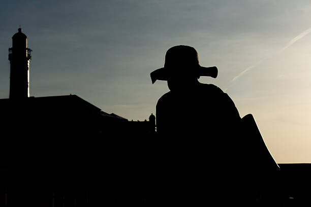Salvador, Bahia, Brazil - December 12, 2025: A man wearing a hat, in silhouette, is seen walking during sunset at Barra. Salvador, Bahia.