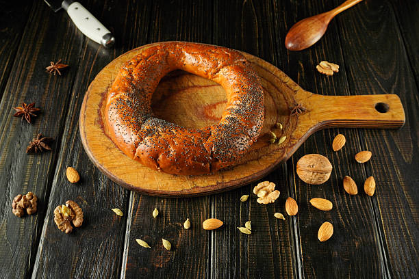 istock Bread shaped like a ring or bagel sits on a wooden board. Nuts and spices are scattered around. A kitchen knife and a wooden spoon are nearby. The scene shows a cozy cooking moment 2252556607