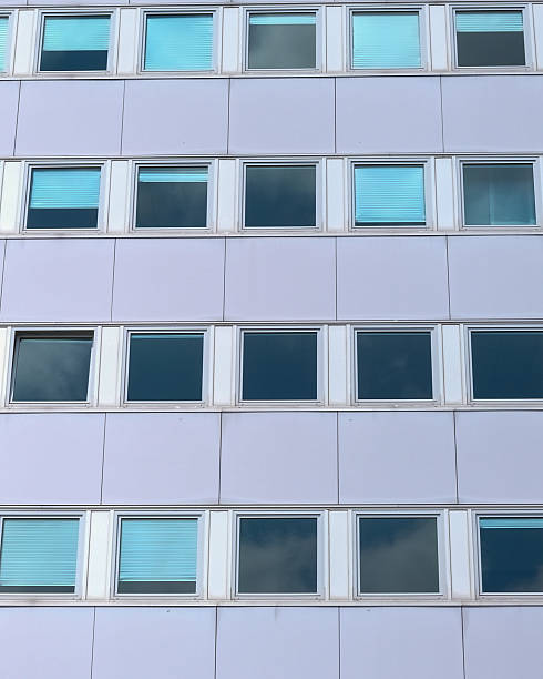 istock Modern building facade featuring rows of windows with reflective surfaces showing clouds and blue sky 2252562338