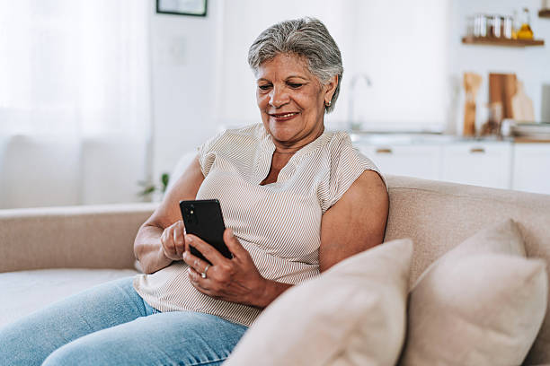 istock Smiling Senior Woman Sitting On Sofa Using Smartphone 2252563224