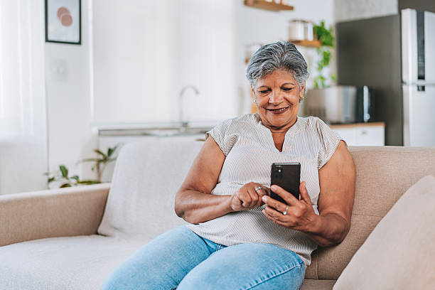 istock Smiling Senior Woman Sitting On Sofa Using Smartphone 2252563231