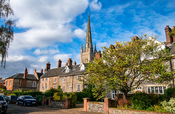 The tower and spire of the lovely 11th century Norwich Cathedral seen behind houses in the Cathedral Close in the beautiful old city of Norwich in Norfolk, Eastern England on an autumn day.
