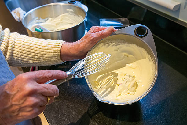 A mature female putting the finishing touches into preparing a cheesecake on a table in a domestic kitchen