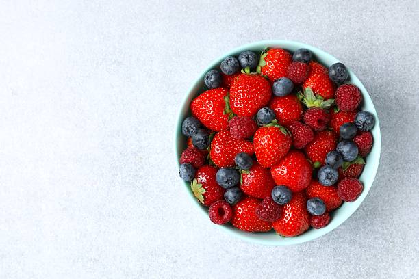 istock Different fresh ripe berries in bowl on grey table, top view 2252565756