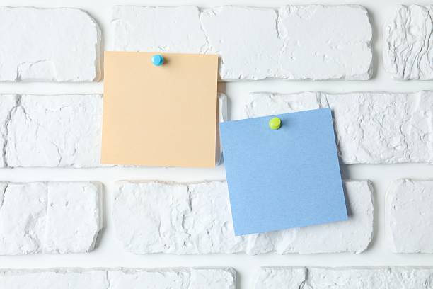istock Colored paper stickers attached with pushpin on a white brick wall 2252565874