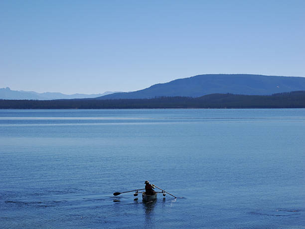View from a boat on a lake with the Bavarian Alps in the background under a bright blue sky, featuring calm water and a small sailboat in the distance.