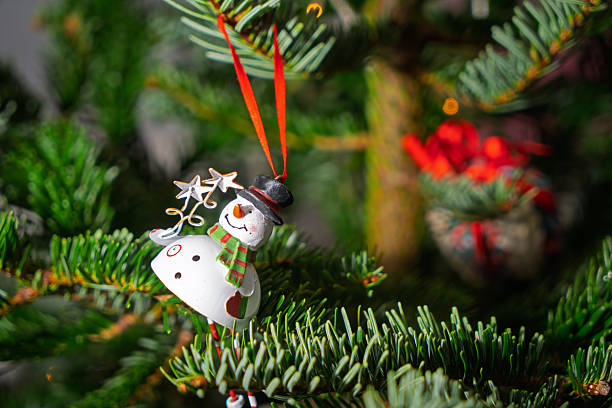istock Snowman ornament hanging on Christmas tree branch with festive decorations and lights 2252573033