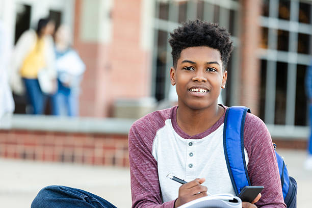 istock Teenage student with backpack writing in notebook and holding a smartphone 2252574105