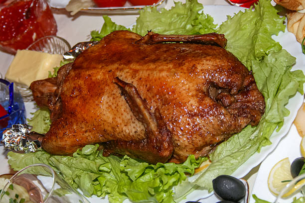 A whole roast duck with a crispy golden-brown skin, served on fresh lettuce leaves on a festive table. A traditional, gourmet poultry dish, perfect for a holiday dinner, celebration, or special occasion. A concept of high-quality, homemade roasted meat for culinary, festive, and hearty dishes.