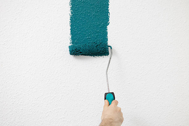 istock A roller in hand paints a white wall in a dark green background 2252577241