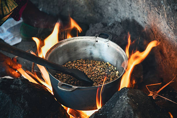 Coffee beans are roasted in a metal pot over an open fire in a traditional kitchen in Uganda