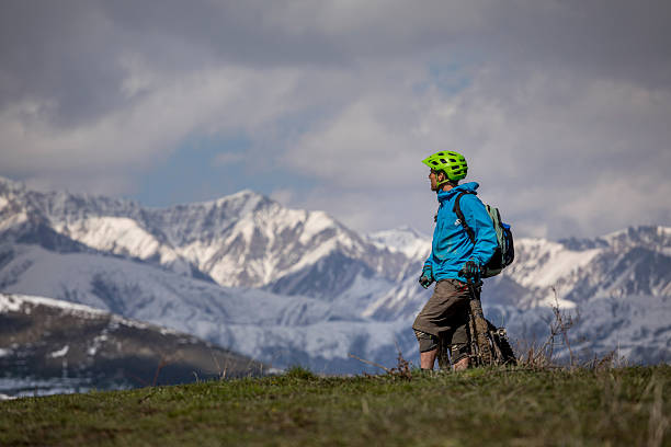 Mountain biker stands in meadow and looks at snowcapped mountains, Greater Caucasus