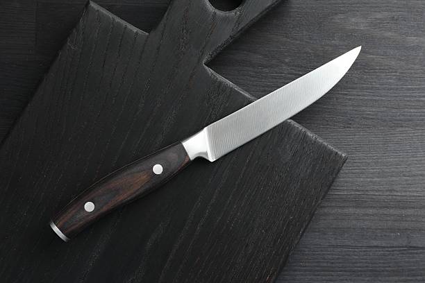 istock One sharp knife and board on black wooden table, top view 2252592538