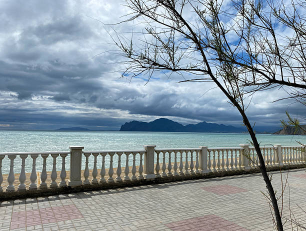 istock Scenic waterfront view with a cloudy sky, featuring a decorative railing and distant mountains, creating a serene coastal atmosphere 2252595576