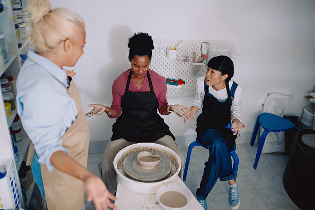 A diverse group of women participating in a pottery class, learning to shape clay on the pottery wheel in a creative studio setting. The image highlights hands-on learning, cultural diversity, and the joy of artistic exploration. Ideal for concepts such as creative workshops, art education, community learning, female empowerment, and multicultural collaboration.